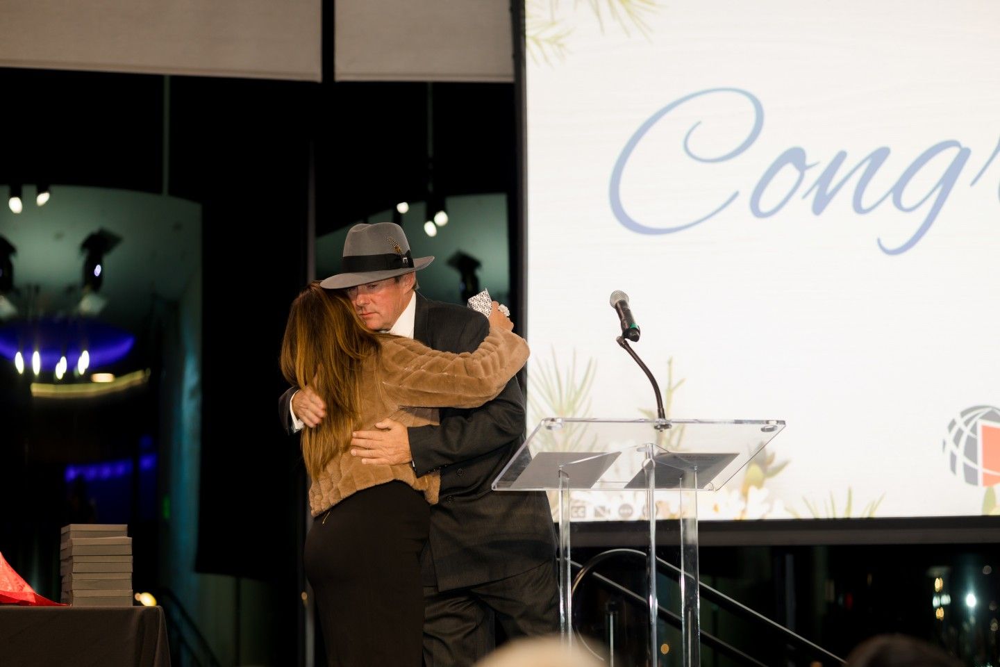 Man in hat and woman hugging at a podium. 