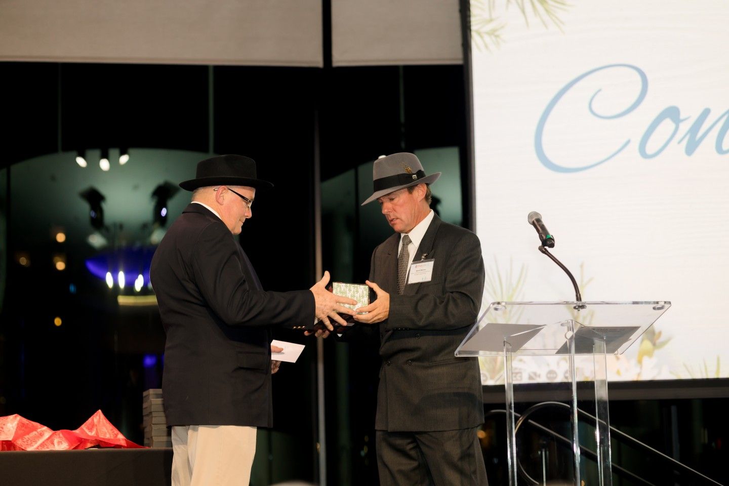 Two men in hats exchanging a gift at an event with a 