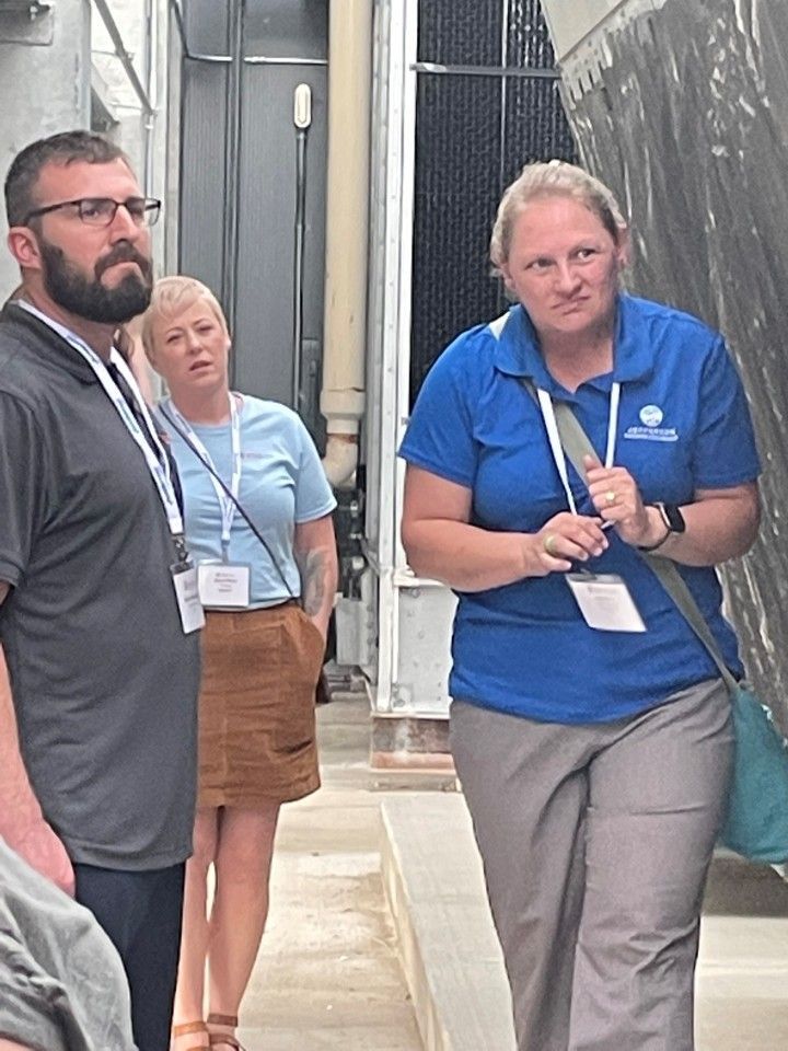 Three people on a tour. A man with a beard, a woman with short hair, and a woman in a blue shirt with a badge.
