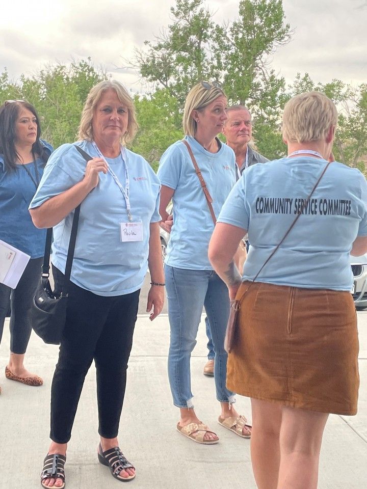 People in light blue shirts, some with lanyards, converse outdoors. One person wears a brown skirt.