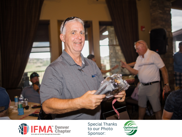 Man holding gift at event; others in background; interior setting.