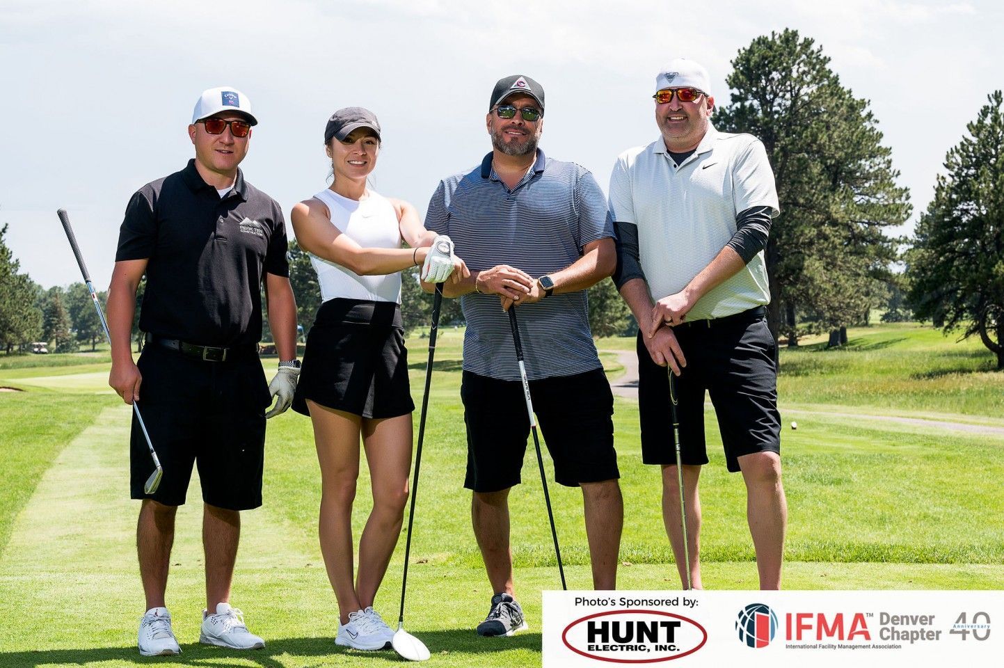 Four people standing on a golf course, posing with golf clubs.