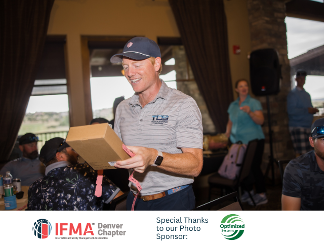 Man in cap smiles, holding gift box at IFMA Denver event.