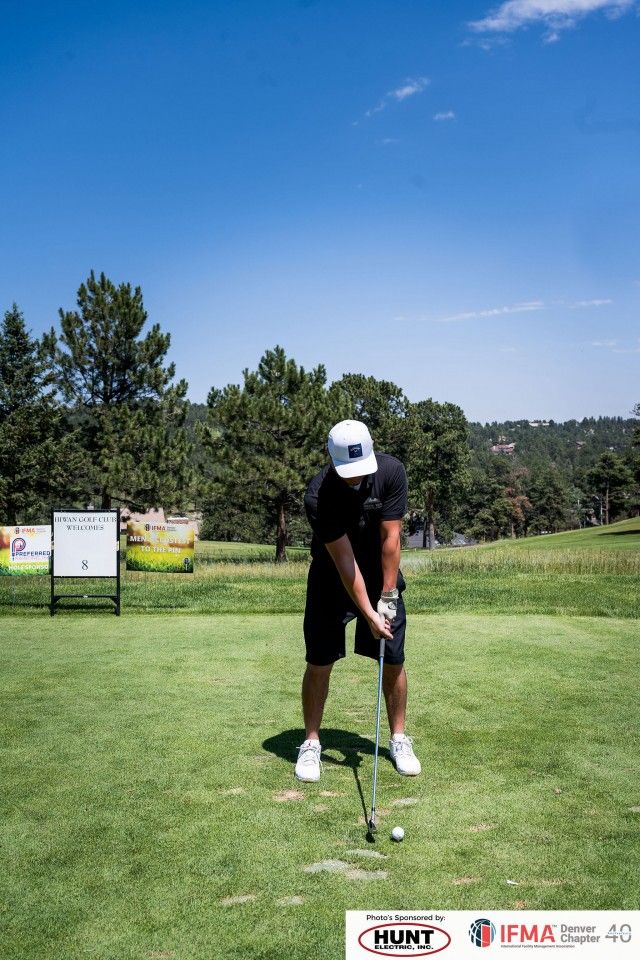 Man in black outfit tees off on a golf course under a blue sky.