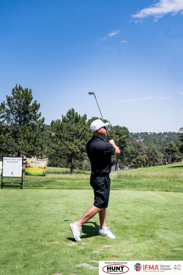 Man swinging golf club on green, sunny day.
