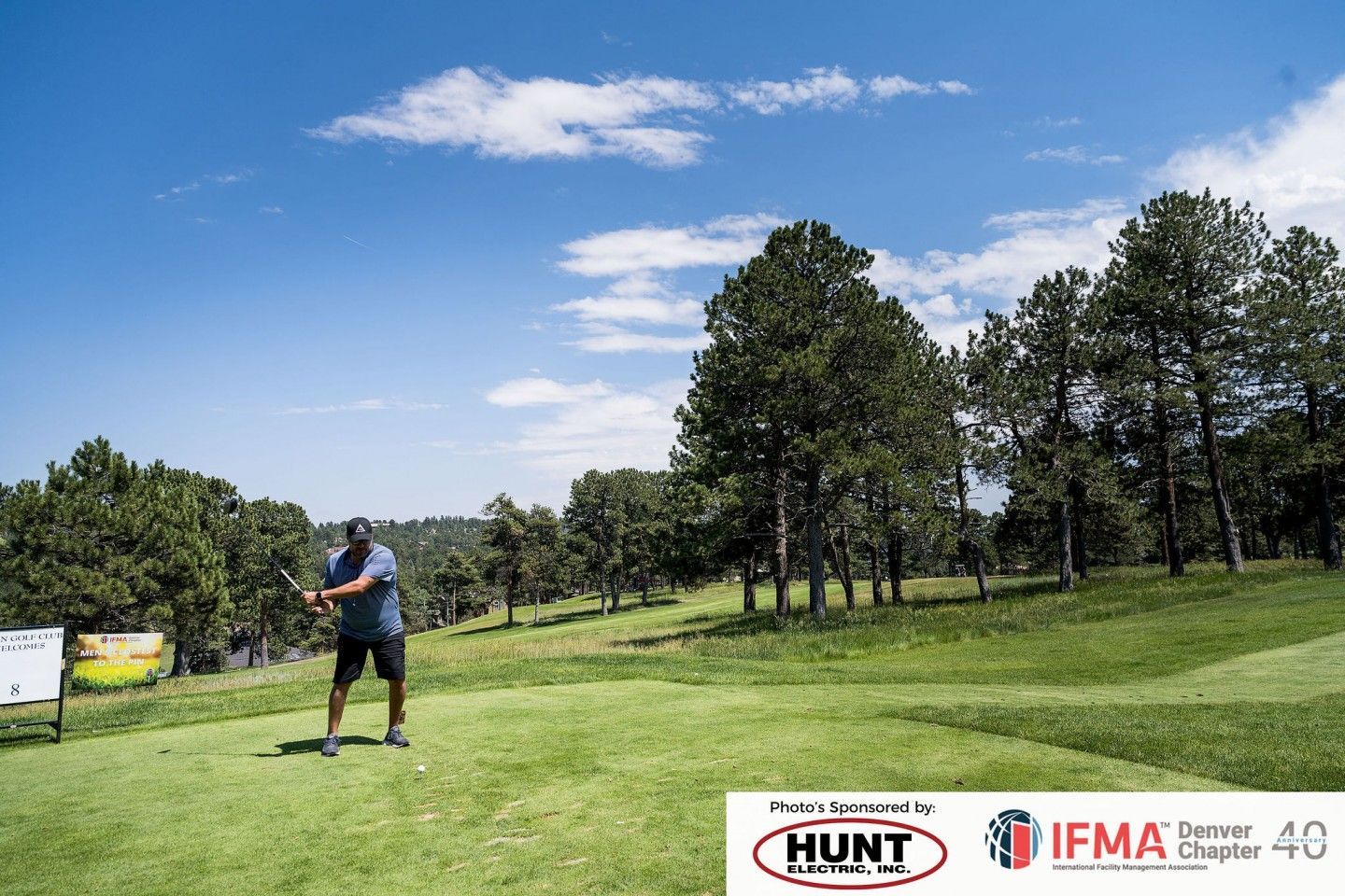 Man tees off on a golf course. Sunny day, green grass, trees.