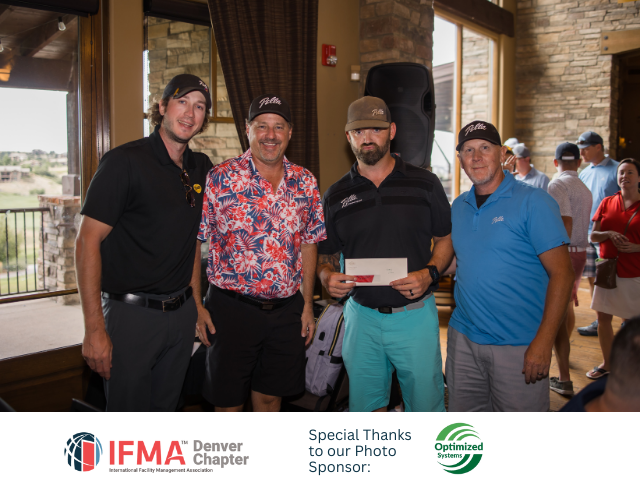 Four men at an event, one holding a check. Outdoors setting.