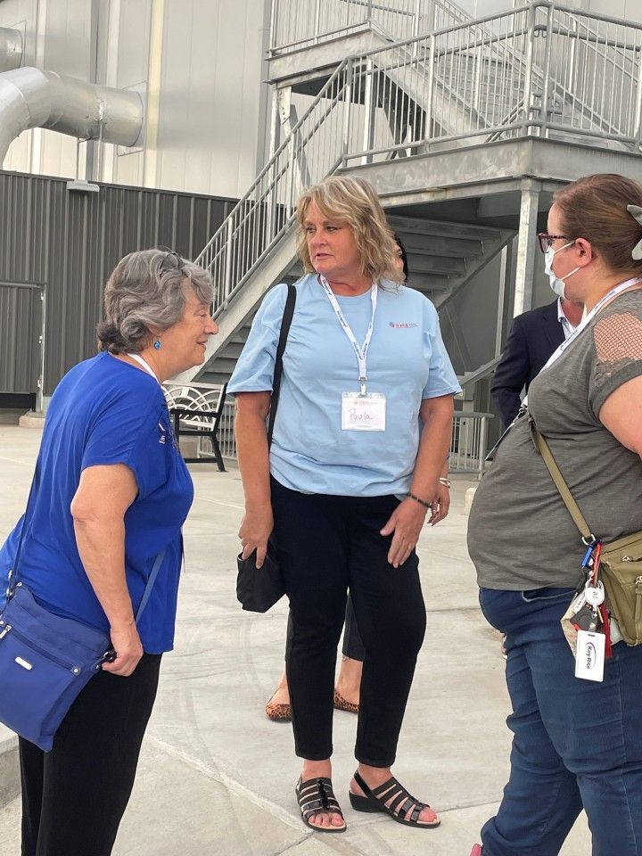 Three women talking outdoors near a metal structure