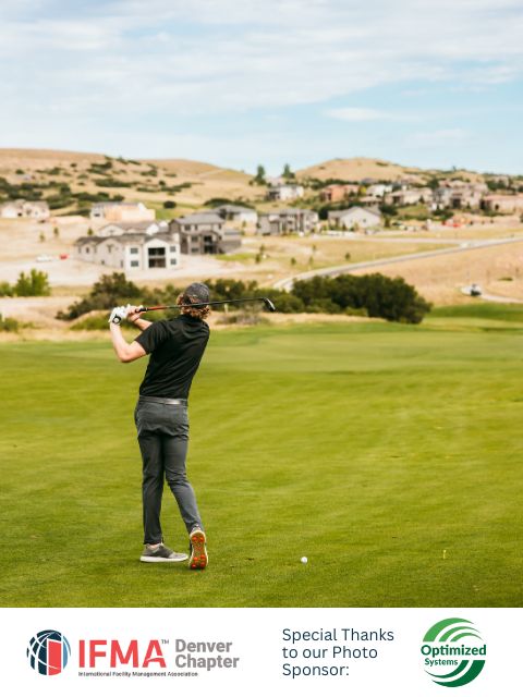 Golfer swinging on a green golf course, with suburban homes in the background. Sunny day.