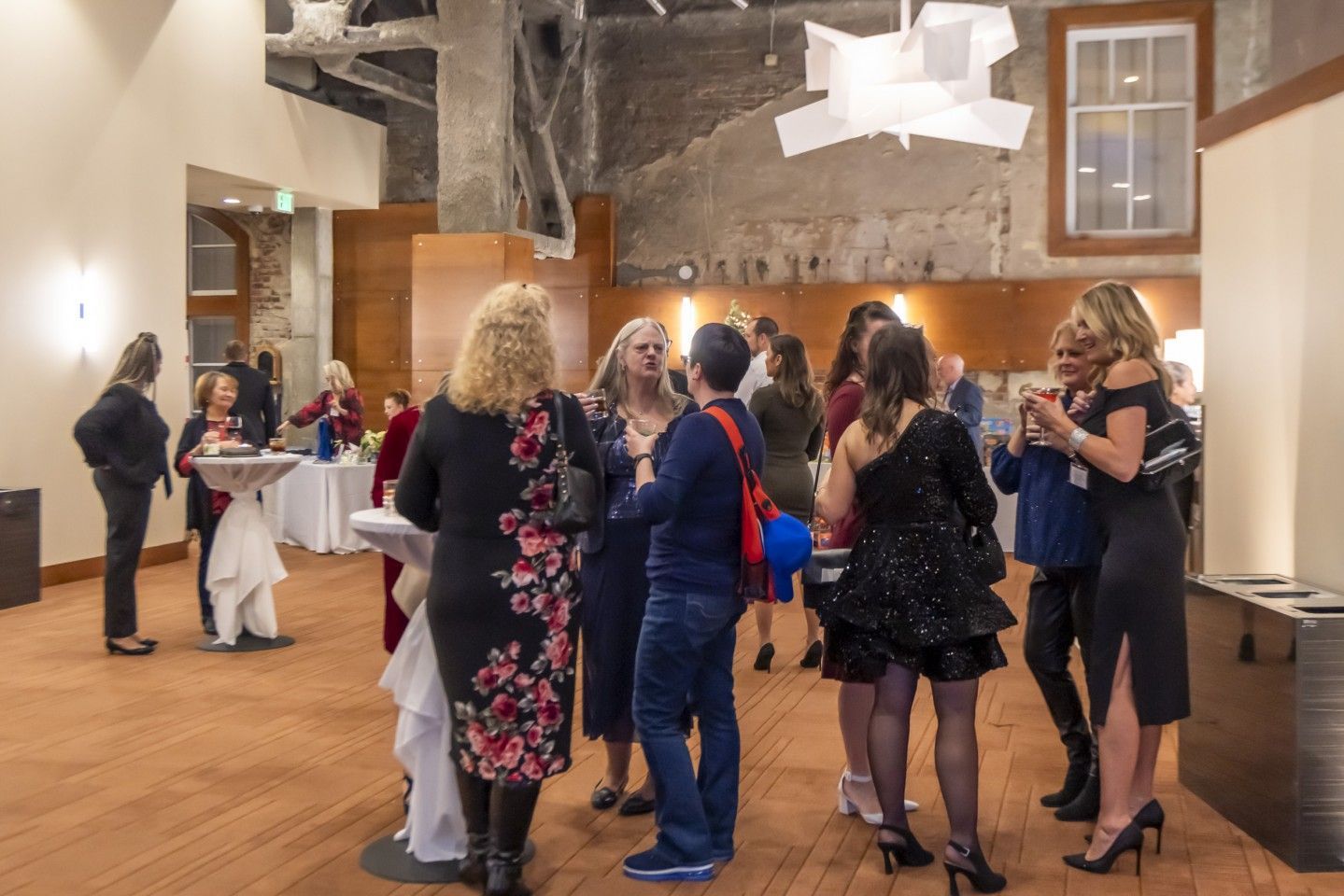 People gathered at an event in a spacious room with wood floors and exposed brick walls, socializing.