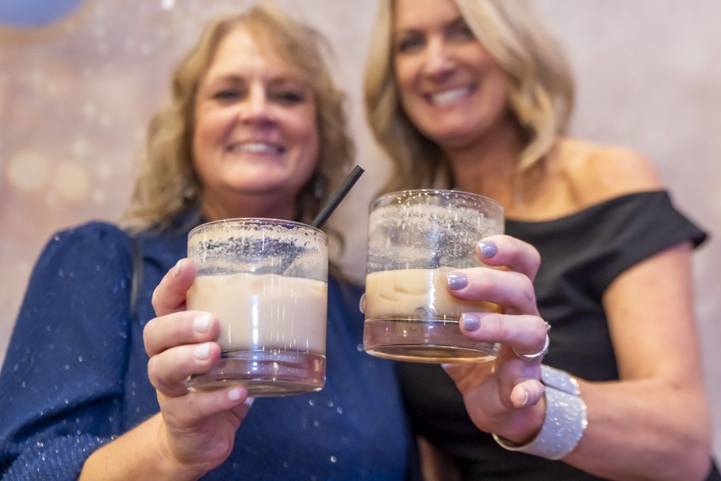 Two women smiling, toasting drinks with sugared rims, in a celebratory setting.