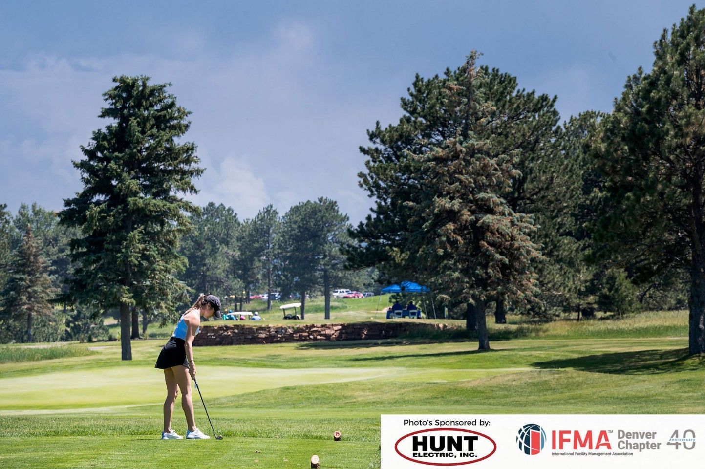 Woman golfing on a green course, trees in the background, under a blue sky.