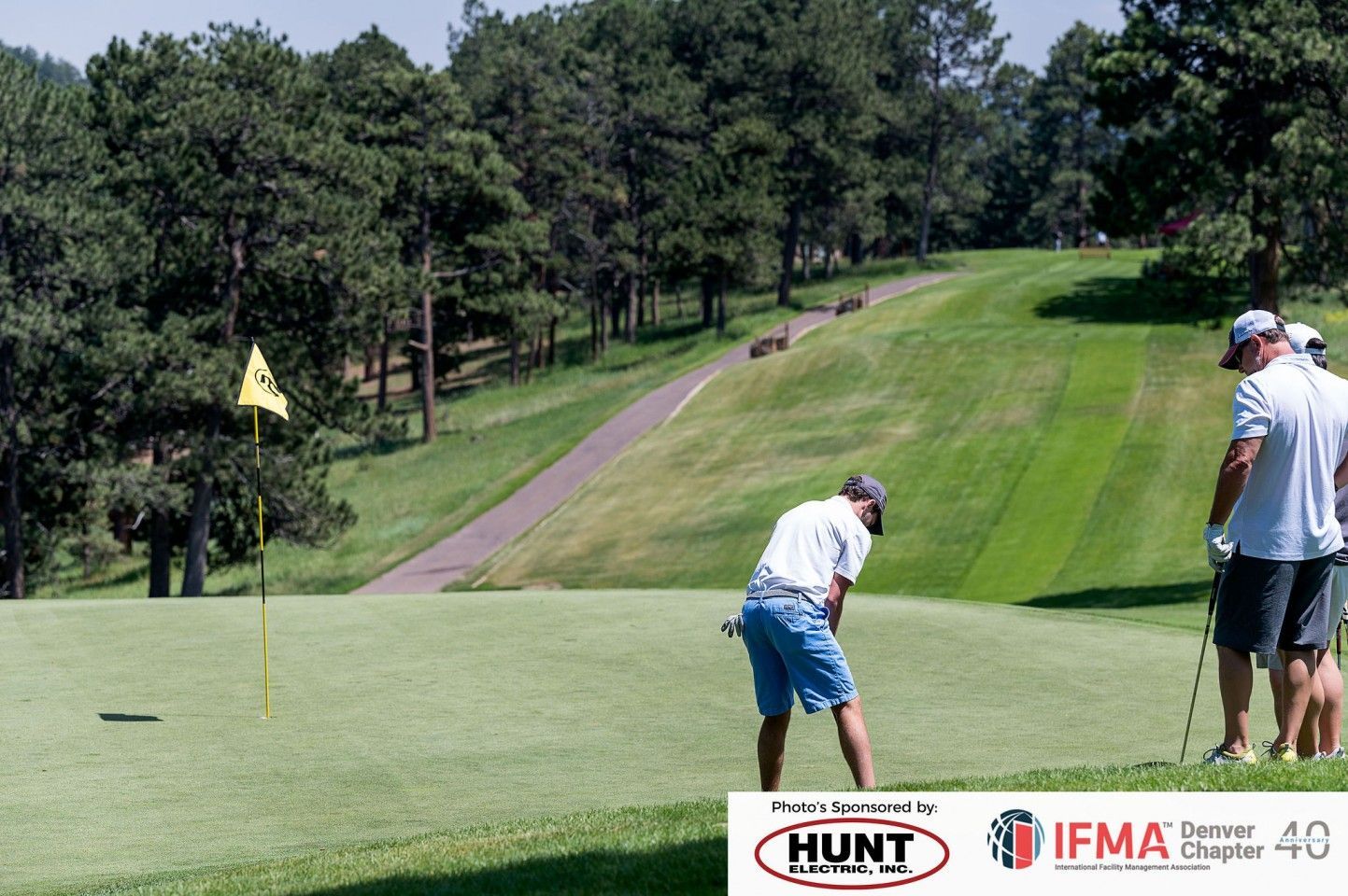 Golfer putting on green, with two other players watching. Golf course, sunny day.