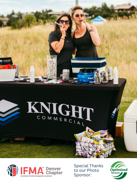 Two women at a Knight Commercial booth smoking cigars. Event outdoors with snacks and supplies on a table.