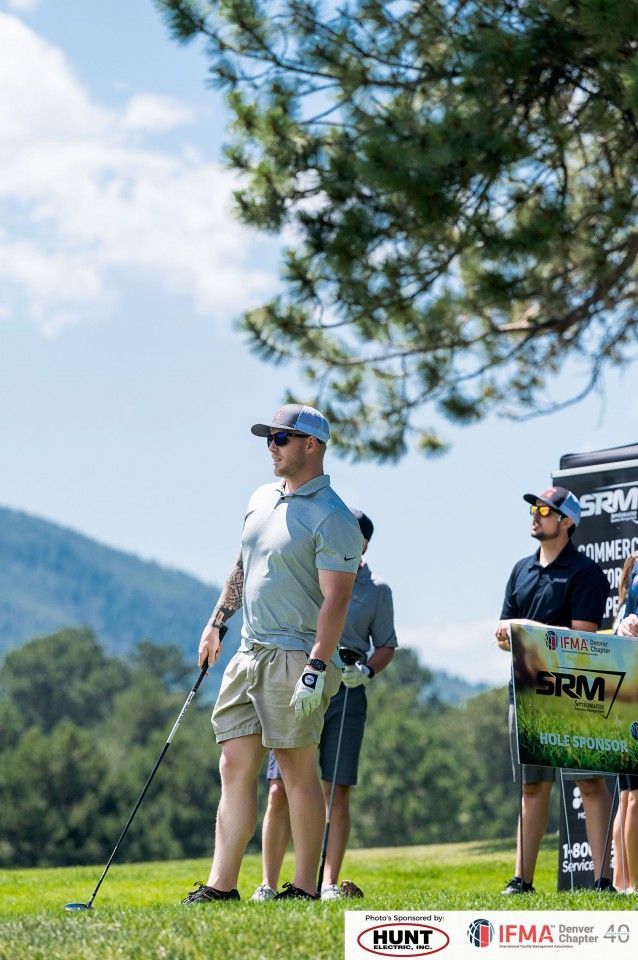 Man on golf course teeing off, wearing sunglasses and hat, with mountain background.