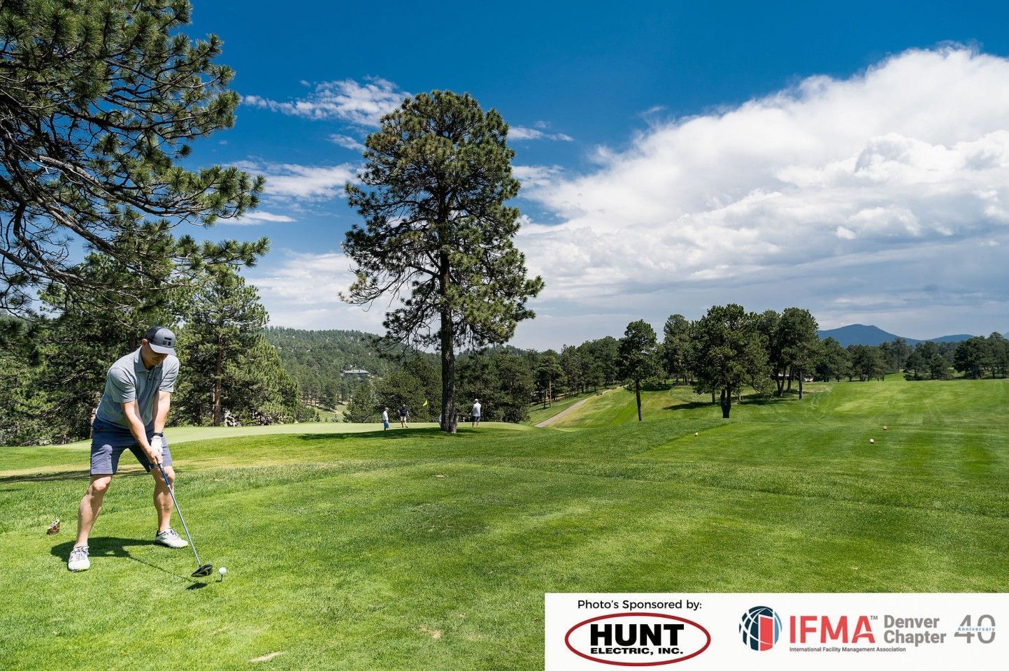 Golfer teeing off on a green golf course under a blue sky with fluffy white clouds.