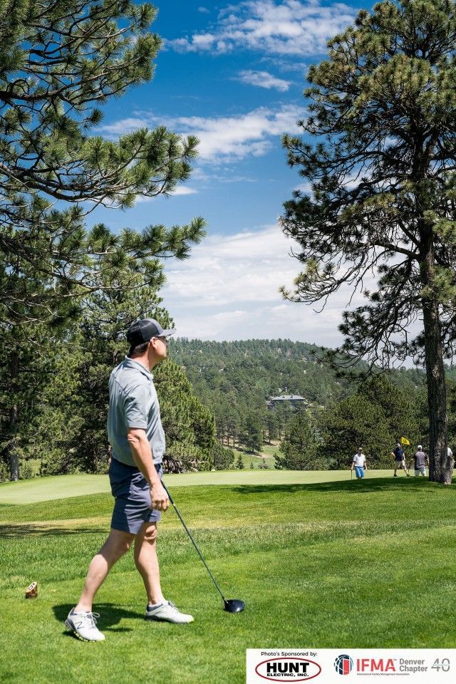 Man on golf course tee box, looking towards fairway. Sunny day, green grass, trees, mountains in background.