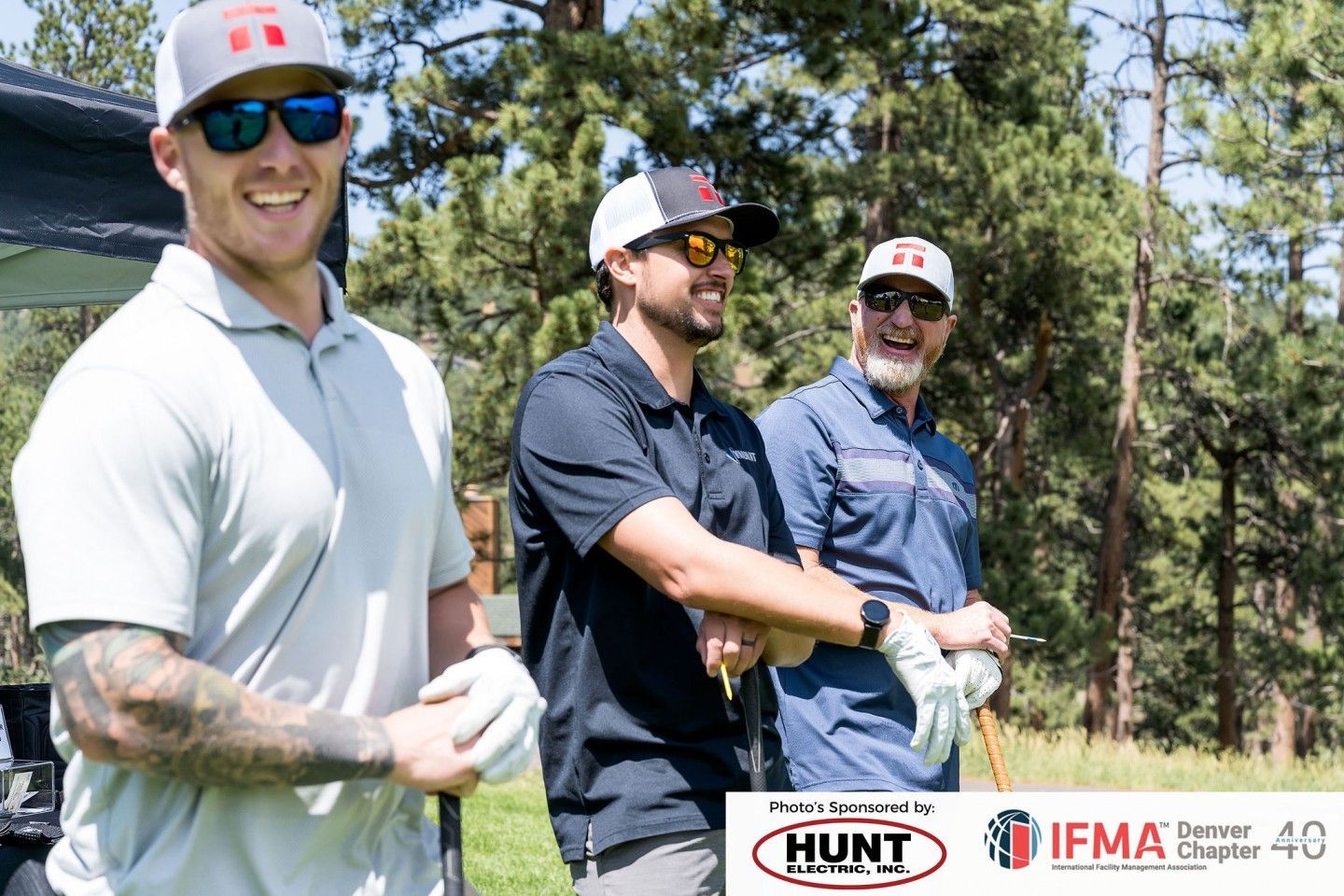 Three men in golf attire smile in a sunny outdoor setting.