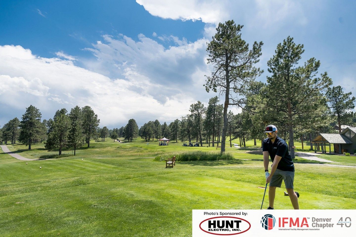 Man golfing on a green course under a blue sky with trees.