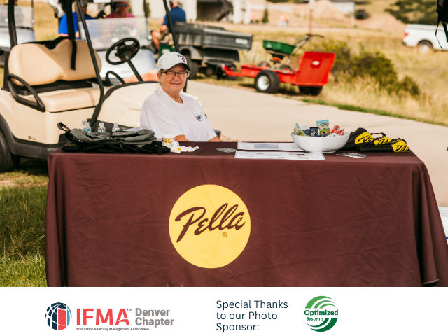 A person sits at a Pella-branded table at an outdoor event near golf carts.