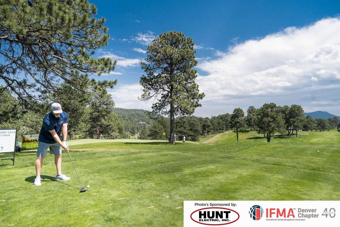 Golfer about to swing club on green golf course under a blue sky.