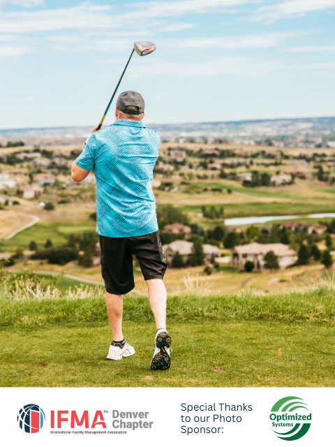 Golfer in blue shirt swings club on golf course with green landscape and sky in background.