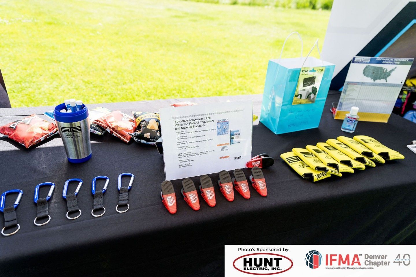 A table with promotional items, including keychains, water bottle, and first aid kits, outdoors in front of grass.