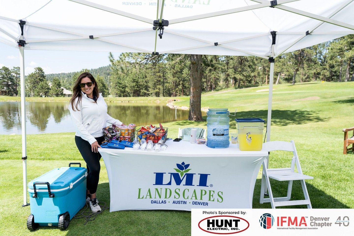 Woman at LMI Landscapes booth, with drinks and snacks, at an outdoor event on a golf course.