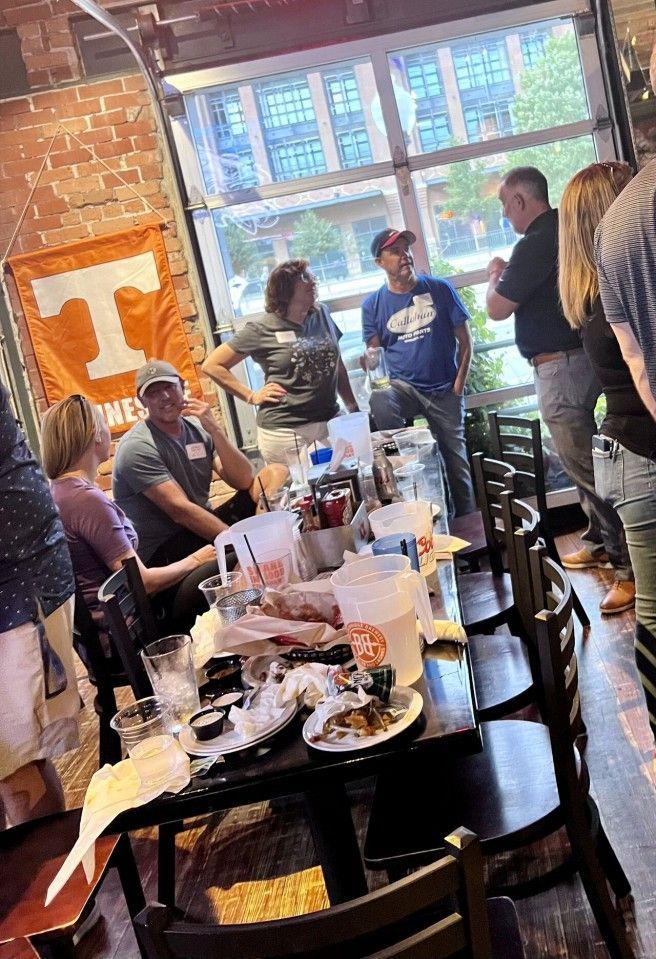 People gathered at a restaurant table with food and drinks. The UT Vols banner hangs nearby.