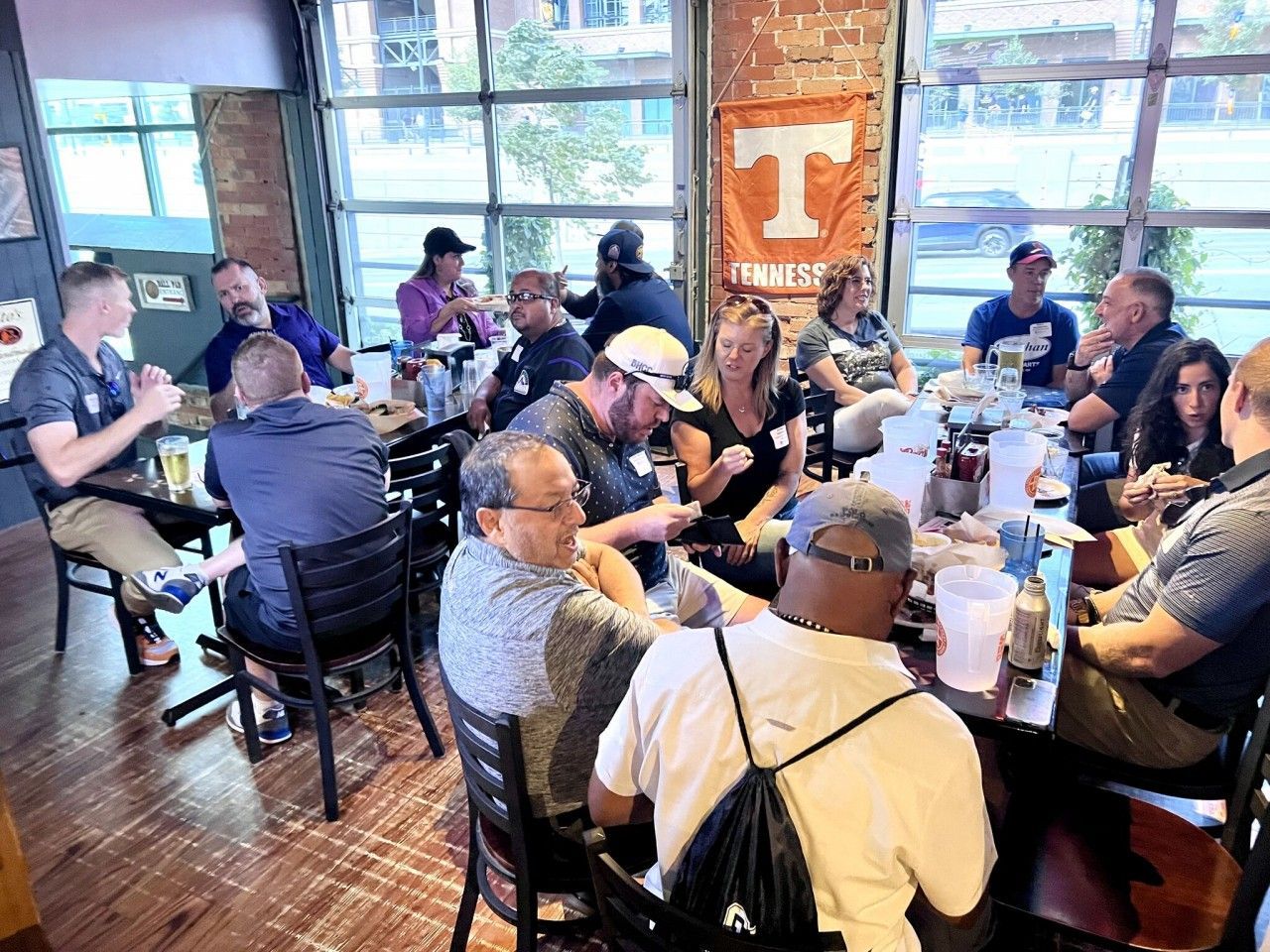Group of people seated at a table in a restaurant, eating and talking. Tennessee Volunteers banner visible.
