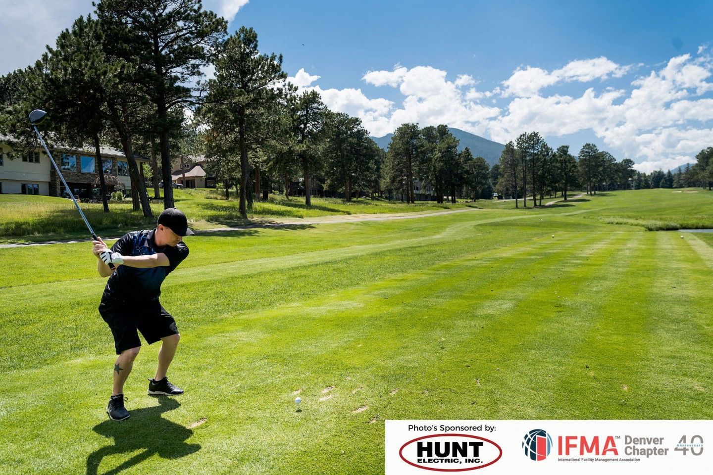 Golfer swinging club on a green course, blue sky, trees in background. Hunt Real Estate and IFMA logos at bottom.