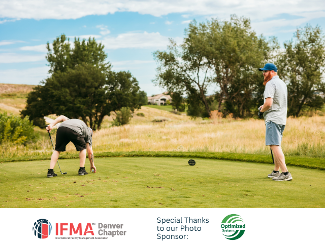 Two men on a golf course. One tees off, the other watches. Sunny day, green grass, trees in the background.