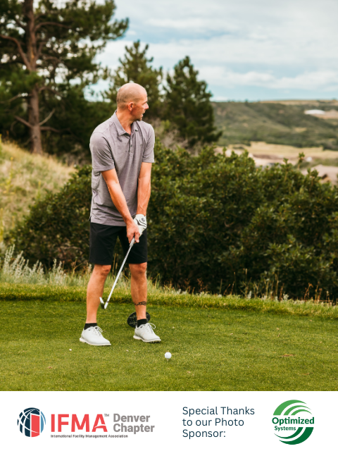 Man in gray shirt and black shorts about to hit a golf ball on a green course.