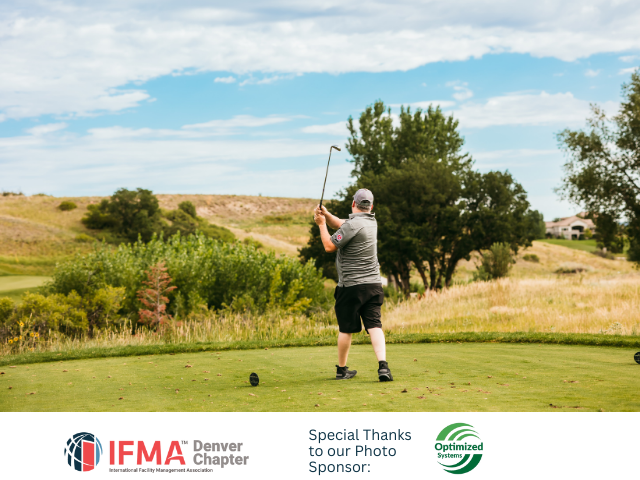 Golfer swinging club on green, with hills and blue sky.