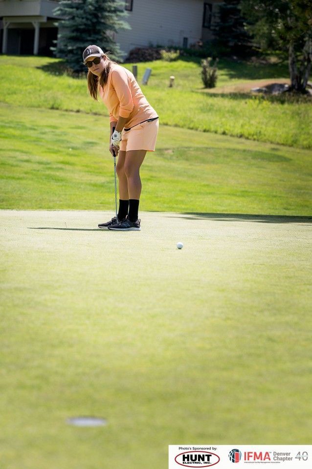 Woman putting golf ball on a green, wearing peach outfit and cap.