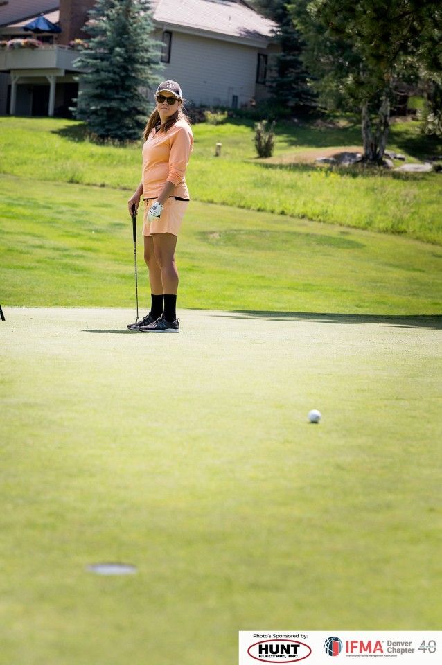 Woman golfing on a green, wearing a light orange outfit, looking at a white ball.