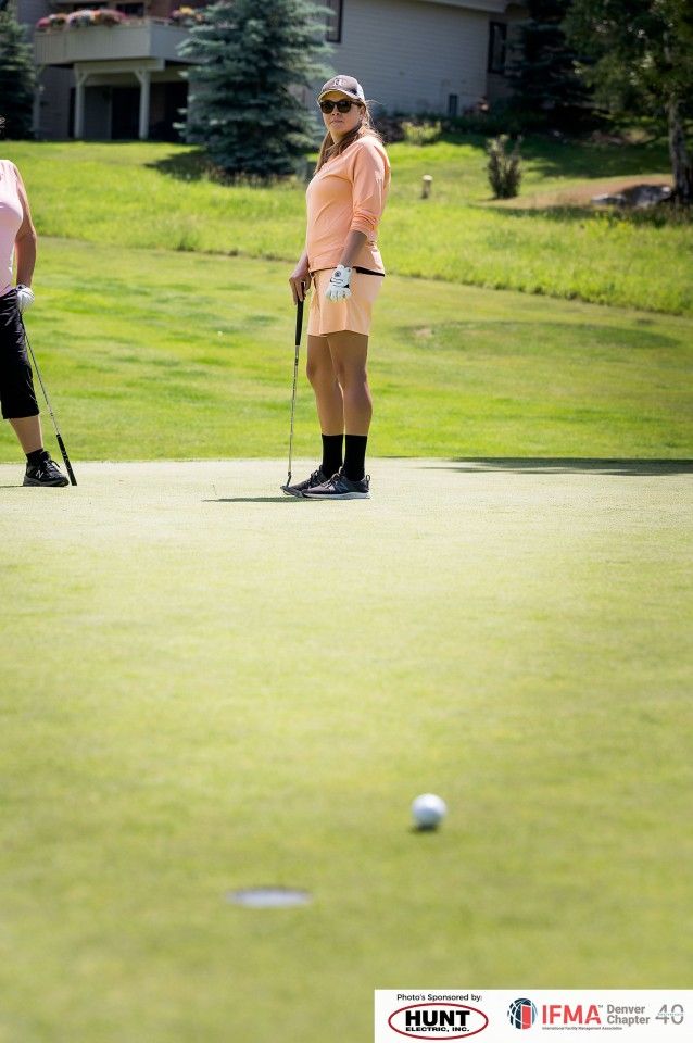 Woman in peach golf attire, putting on a green. Sunny day, golf course setting.