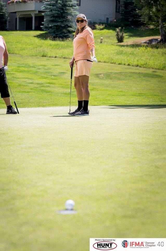 Woman on a golf course putting the ball, wearing peach outfit, sunny day.