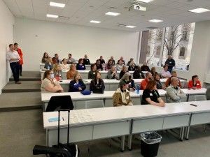 A classroom with people seated at desks; a presentation is likely in progress.