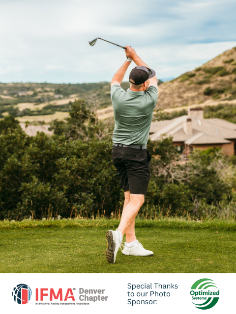 Golfer swings a club on a green course with scenic hills in the background.