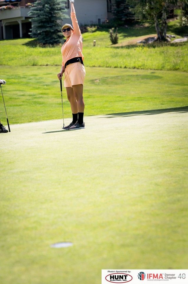Person in peach-colored outfit raises arm in celebration on a green golf course.