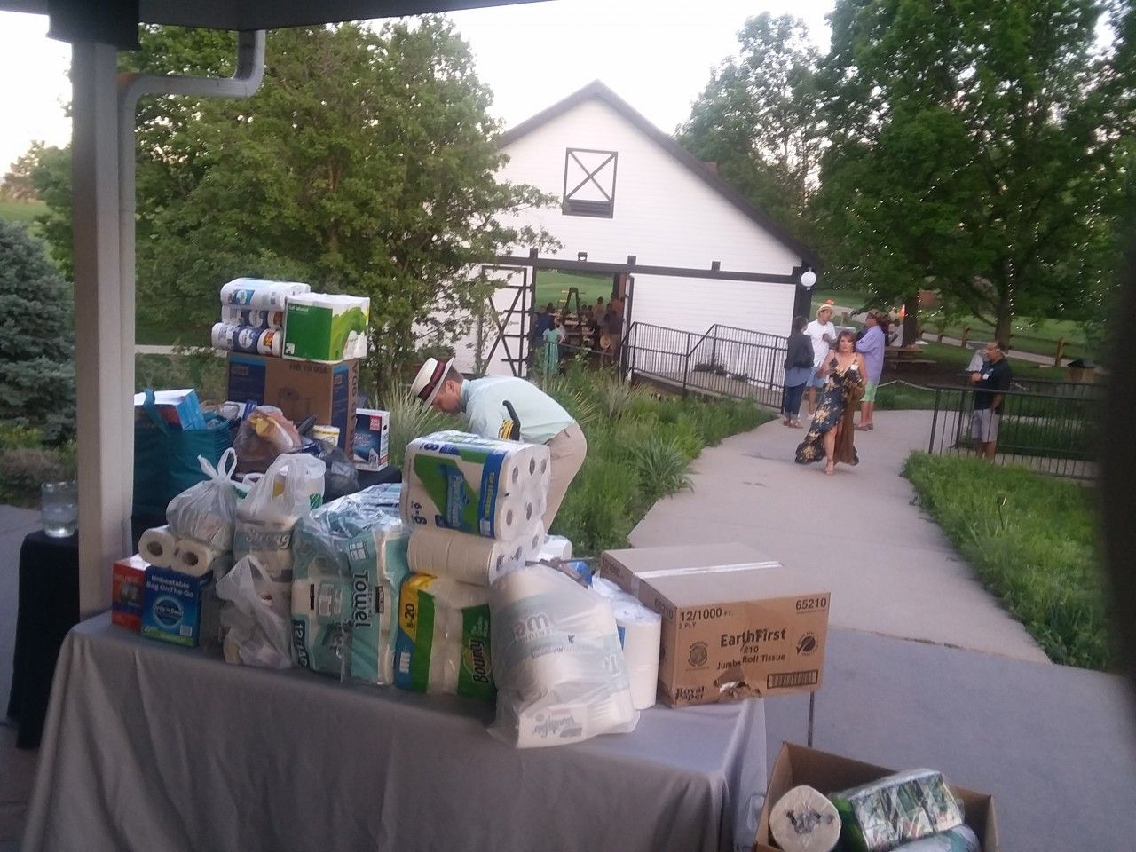 Table with supplies, person at table, people near a white barn, outdoors.