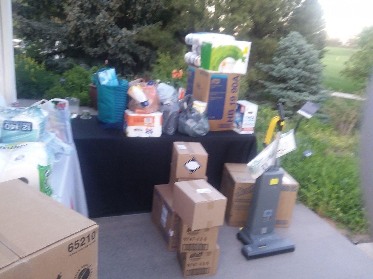 A collection of donations, including boxes of supplies and a vacuum, arranged on a table outdoors.