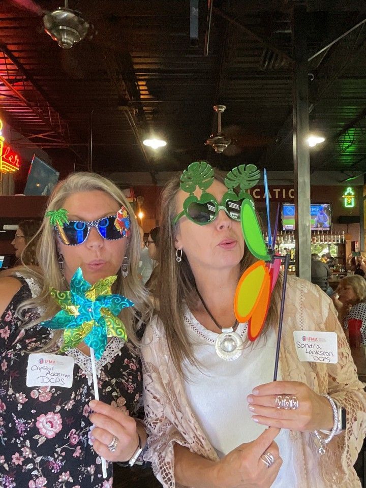 Two women posing, wearing novelty glasses and holding props. Inside a restaurant.