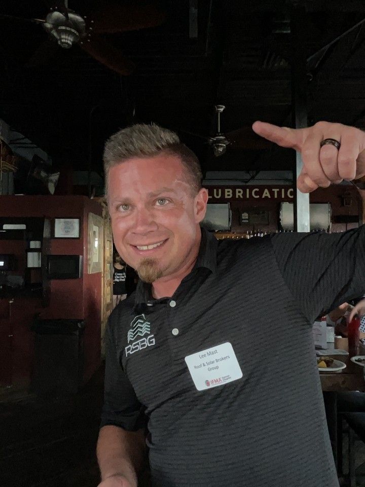 Man points up, smiling, wearing a black shirt with a name tag, in a restaurant setting.