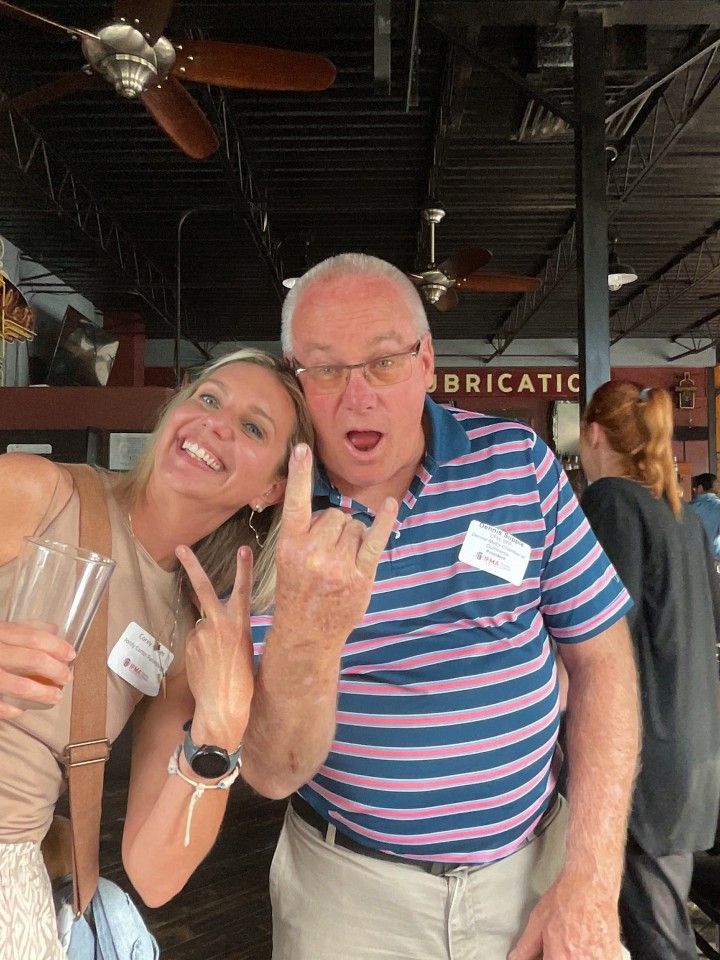 Woman and man posing for photo, both giving hand gestures. Man is wearing striped shirt, open mouth.
