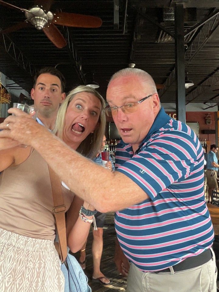Three people making surprised faces while looking at a camera; outdoors under a patio roof.