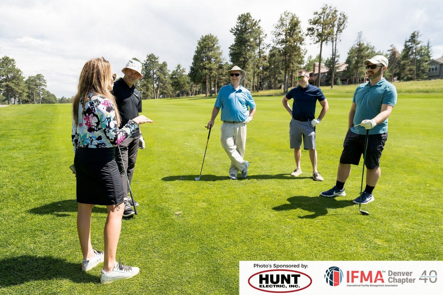 Group of golfers on a green field. Woman facing the group, holding a document, gesturing with her hand.