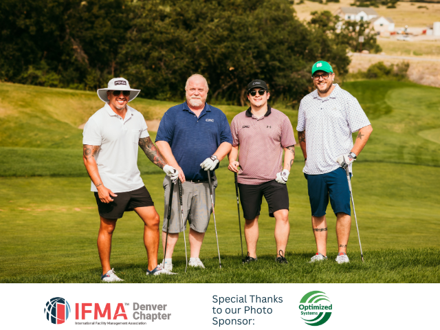 Four men standing on a golf course holding clubs, smiling.