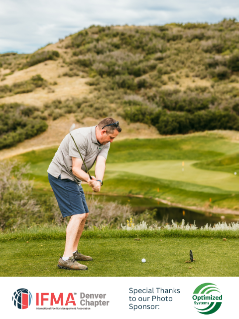 Man in shorts swings golf club on green, course with hills in background.